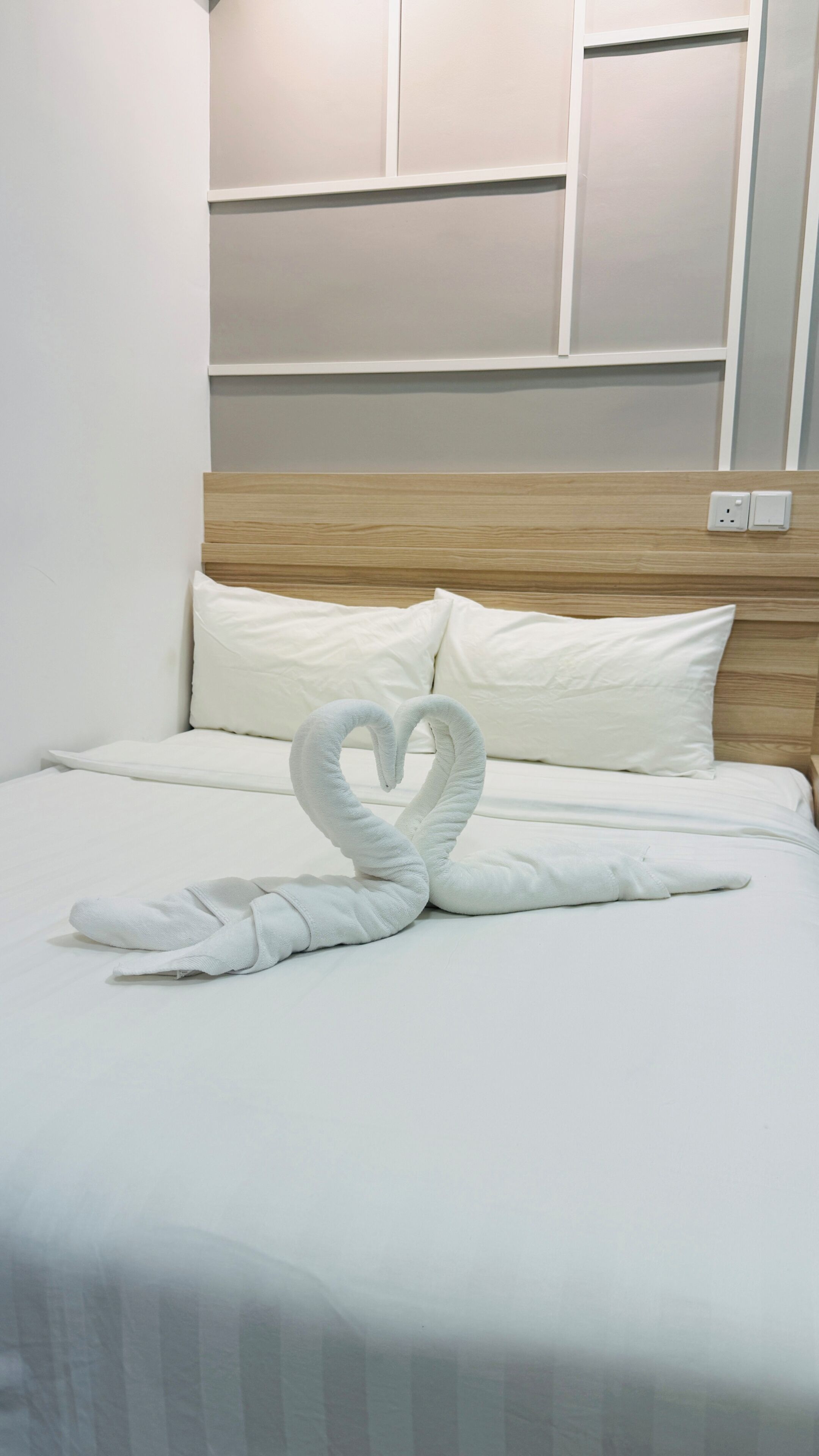 A neatly made bed with a heart-shaped towel arrangement and a wooden headboard.