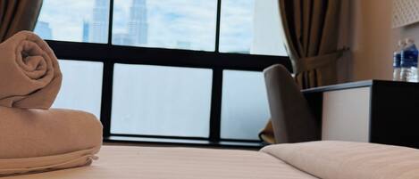 A hotel room with a bed, a desk, a chair, and a view of a cityscape through a large window.