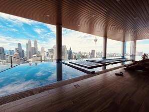 A rooftop infinity pool with a city skyline view, wooden deck, and large columns. - The Colony By Infinitum Flixses (Kuala Lumpur)