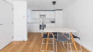 Eine moderne Küche mit weißen Schränken, einem eingebauten Ofen und einem Essbereich mit weißem Tisch und Stühlen.