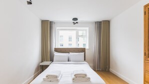 Ein Hotelzimmer mit Bett, Nachttisch, einem Fenster mit Vorhängen und einem Holzschrank.