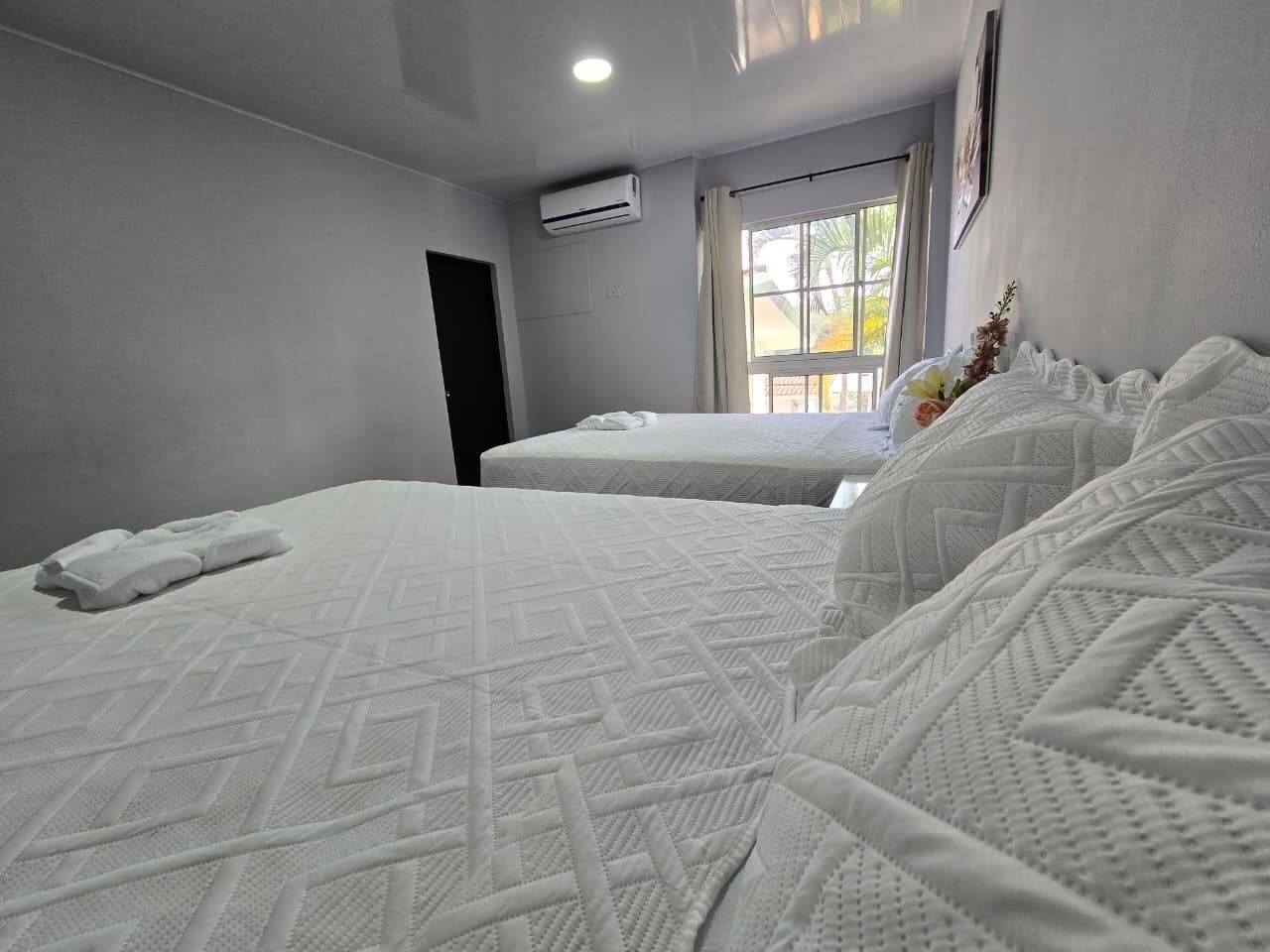 Une chambre d’hôtel avec deux lits, une fenêtre donnant sur un paysage agréable, un appareil de climatisation et une porte.