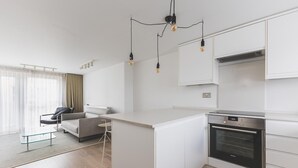 Una cucina moderna con mobili bianchi, forno a incasso e zona pranzo con tavolo in vetro e divano.