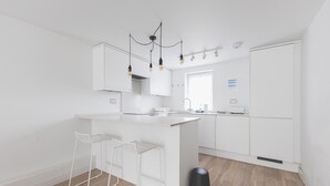 Una cucina moderna con mobili bianchi, un'isola centrale con sgabelli da bar, un cestino nero e un lampadario a sospensione.