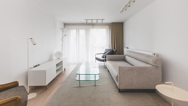 Un soggiorno moderno con un tavolino in vetro, un divano grigio, un mobile contenitore bianco e una lampada da terra.