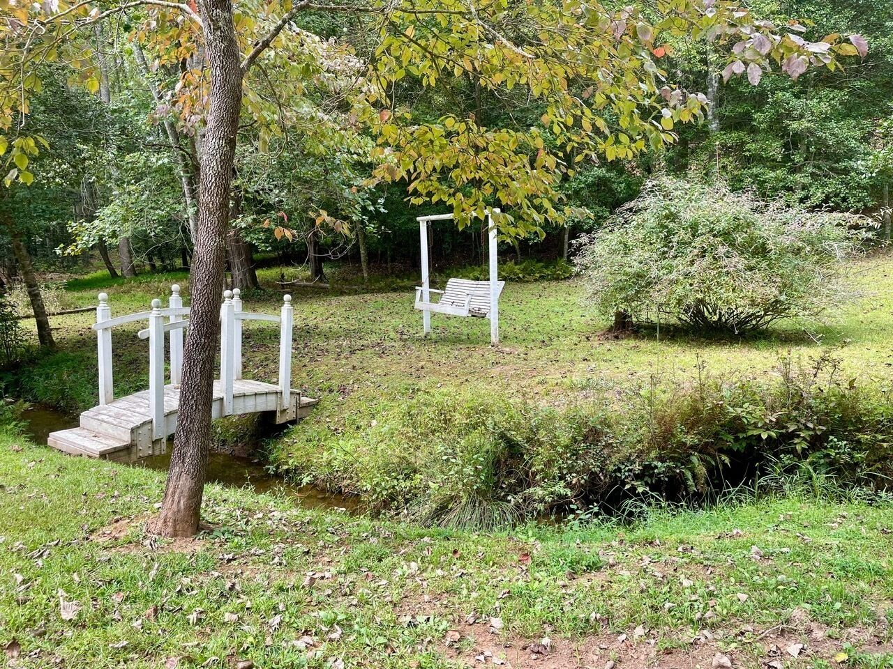 Un parco con un ponte di legno, una panchina bianca e un piccolo corso d'acqua.