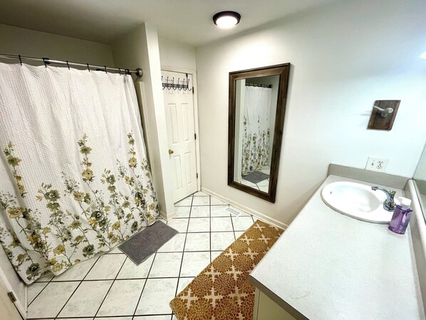 A bathroom with a shower curtain, a mirror, a sink, and a patterned mat.