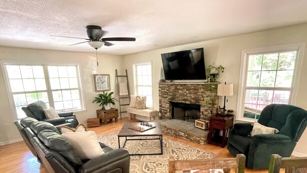 A living room with a stone fireplace, a flat-screen TV, a ceiling fan, and a large window. - Etowah Valley Ranch - Peaceful, private, and serene!  CLose to everything! (Dahlonega)