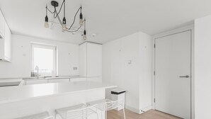 A modern kitchen with a large island, white bar stools, and a chandelier. - Cozy Belgravia Base - Walk to Victoria/Sloane (London)