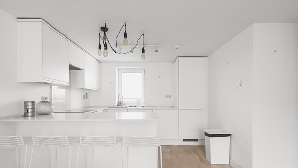 A modern kitchen with white cabinetry, a central island with bar stools, and a pendant light fixture. - Cozy Belgravia Base - Walk to Victoria/Sloane (London)