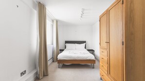 A bedroom with a bed, a wardrobe, and a window with curtains. - Cozy Belgravia Base - Walk to Victoria/Sloane (London)