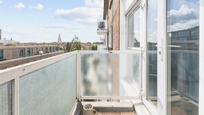 A balcony with a view of a cityscape, including a church spire, and a window with a metal grill. - Cozy Belgravia Base - Walk to Victoria/Sloane (London)