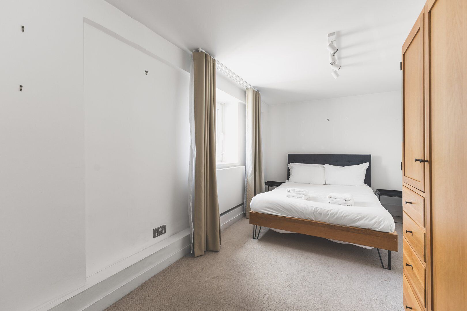 A bedroom with a bed, a wardrobe, a nightstand, and a window with curtains.