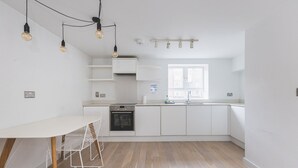 A modern kitchen with white cabinetry, a built-in oven, a sink, and a dining area with a white table and chairs.