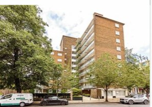 Un immeuble moderne à plusieurs étages, doté d’une façade en briques, entouré d’arbres et bordé de voitures garées.