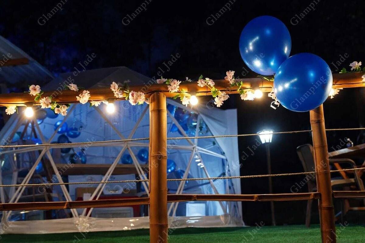 Un espace extérieur aménagé pour les événements, agrémenté d’une structure transparente, de guirlandes lumineuses et de ballons.