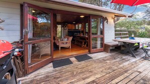 Eine Holzhütte mit einer Terrasse, einem Essbereich und einer Küche, die durch Glastüren zu sehen ist.