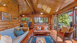 Ein gemütliches Blockhaus-Interieur mit Holzbalkendecke, einer Essecke mit Tisch für vier Personen, einer Couch und Korbstühlen.