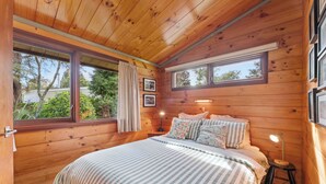 Ein Schlafzimmer mit Holzvertäfelung, einem Bett, zwei Fenstern und einem Nachttisch mit Lampe.