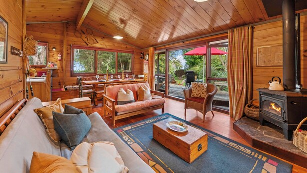Ein gemütliches Blockhaus-Interieur mit Holzbalkendecke, einer Sofagarnitur, einem Esstisch und einem Kamin.