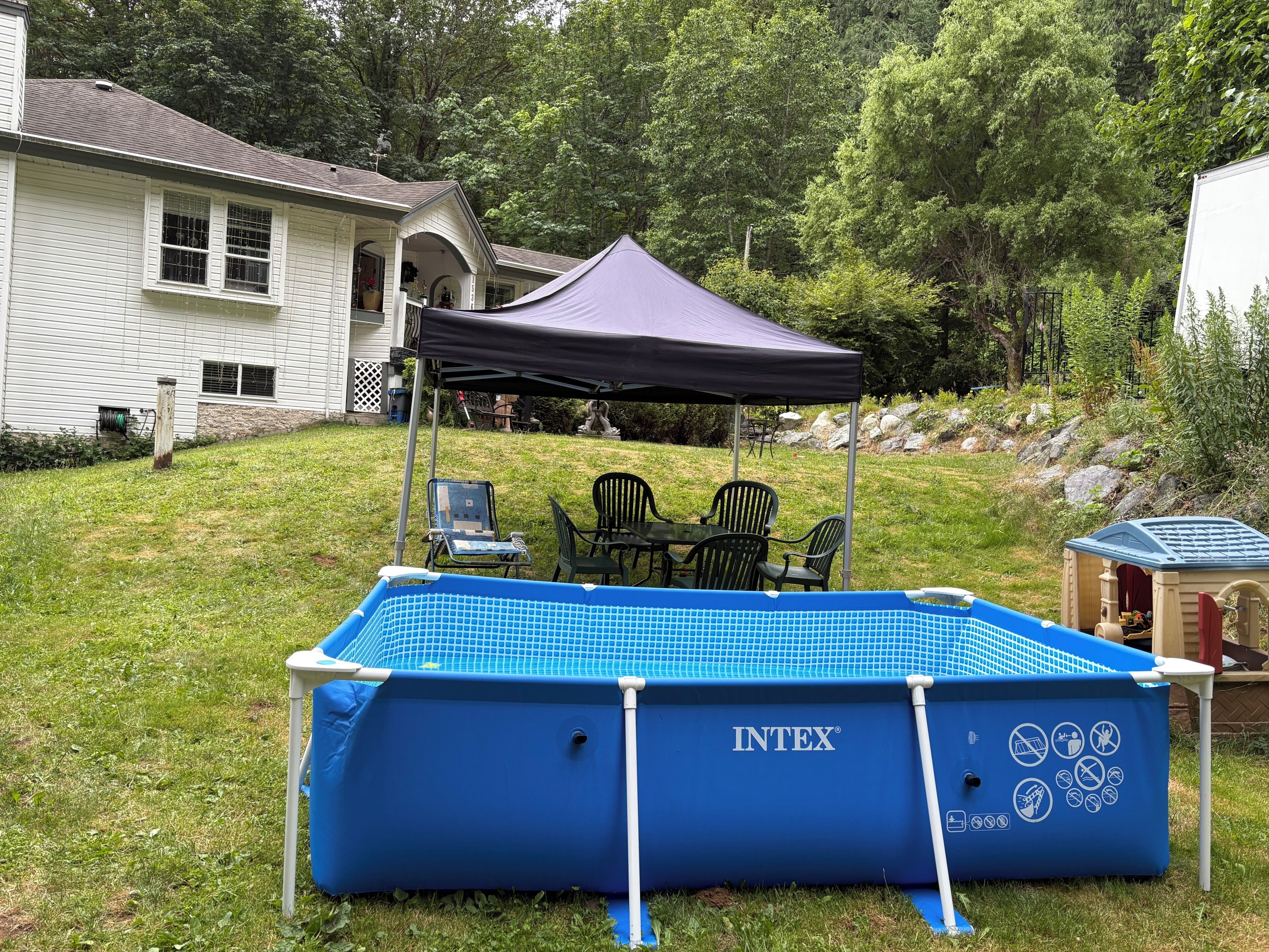 En trädgård med en blå uppblåsbar pool, ett täckt utebord och stolar.