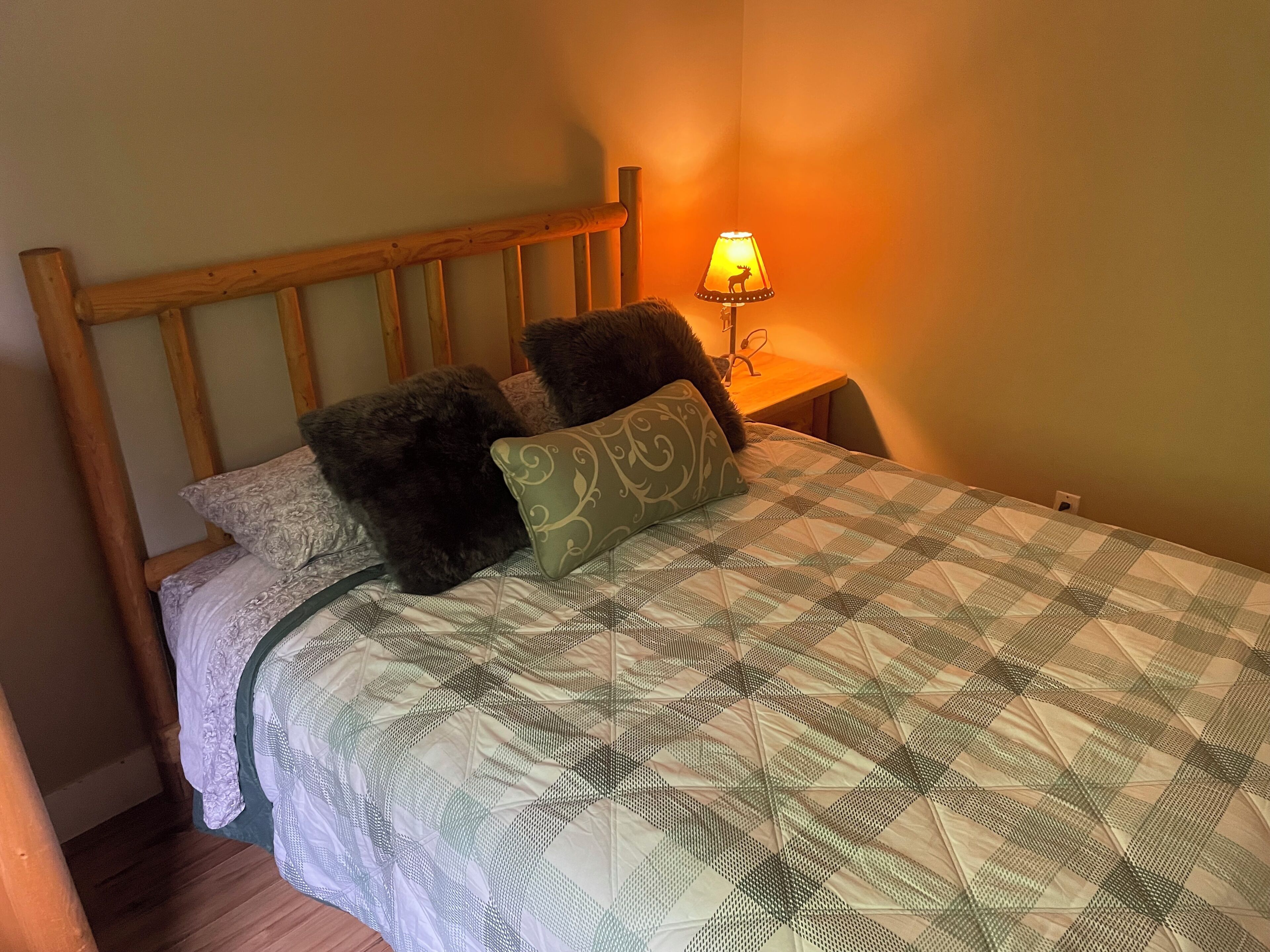 Een bed met een geruit quilt, twee kussens en een houten hoofdbord.