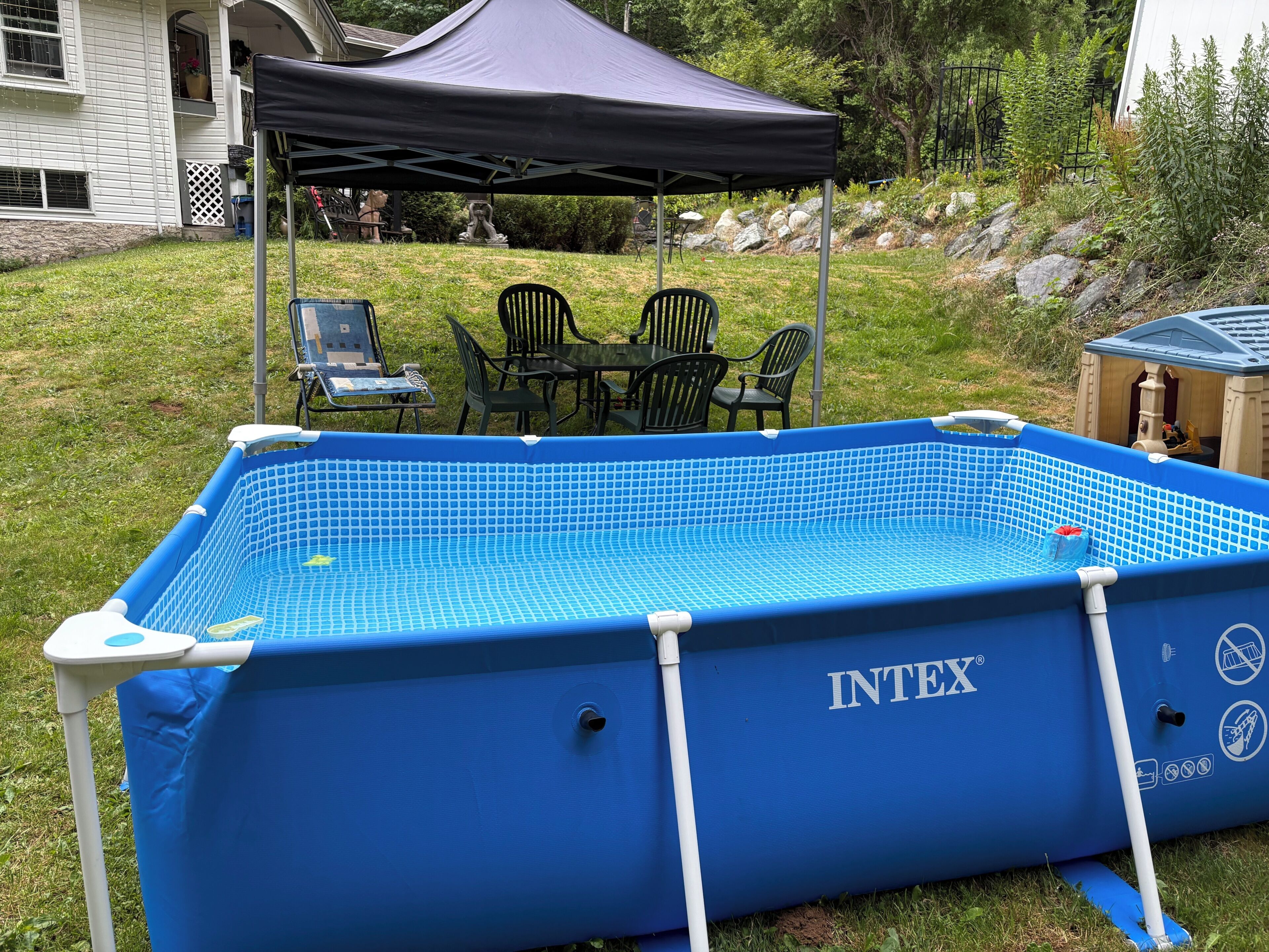 Una piscina inflable INTEX con un porche cubierto, muebles de exterior y una casita de juegos.
