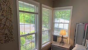 A bedroom with two windows, a bedside table with a lamp, a bed with a patterned bedspread, and a dresser.
