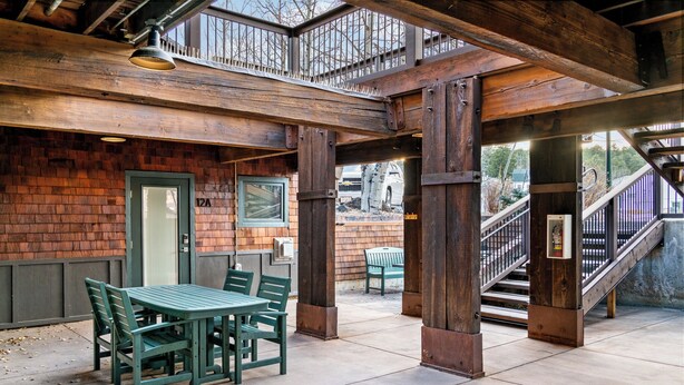 An outdoor patio area with a wooden table and chairs, a staircase, and a view of the street.