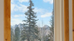 A room with a large window offering a view of a forest and mountains.