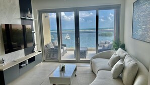 Ein modernes Wohnzimmer mit großem Fernseher, einer Couch, einem Couchtisch und Meerblick durch große Schiebetüren.
