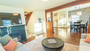 A spacious living room with a fireplace, a dining area, and a kitchen in the background. - Quarter 54 (Palmer)