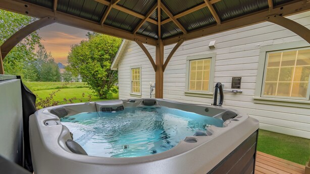 A hot tub under a wooden pergola with a view of a house and greenery. - Quarter 54 (Palmer)