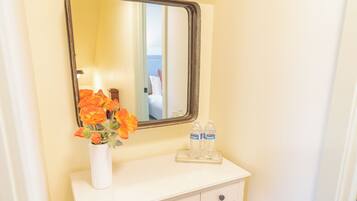 A bathroom with a white vanity, a mirror, and a vase with flowers. There are two bottles of water on the vanity.