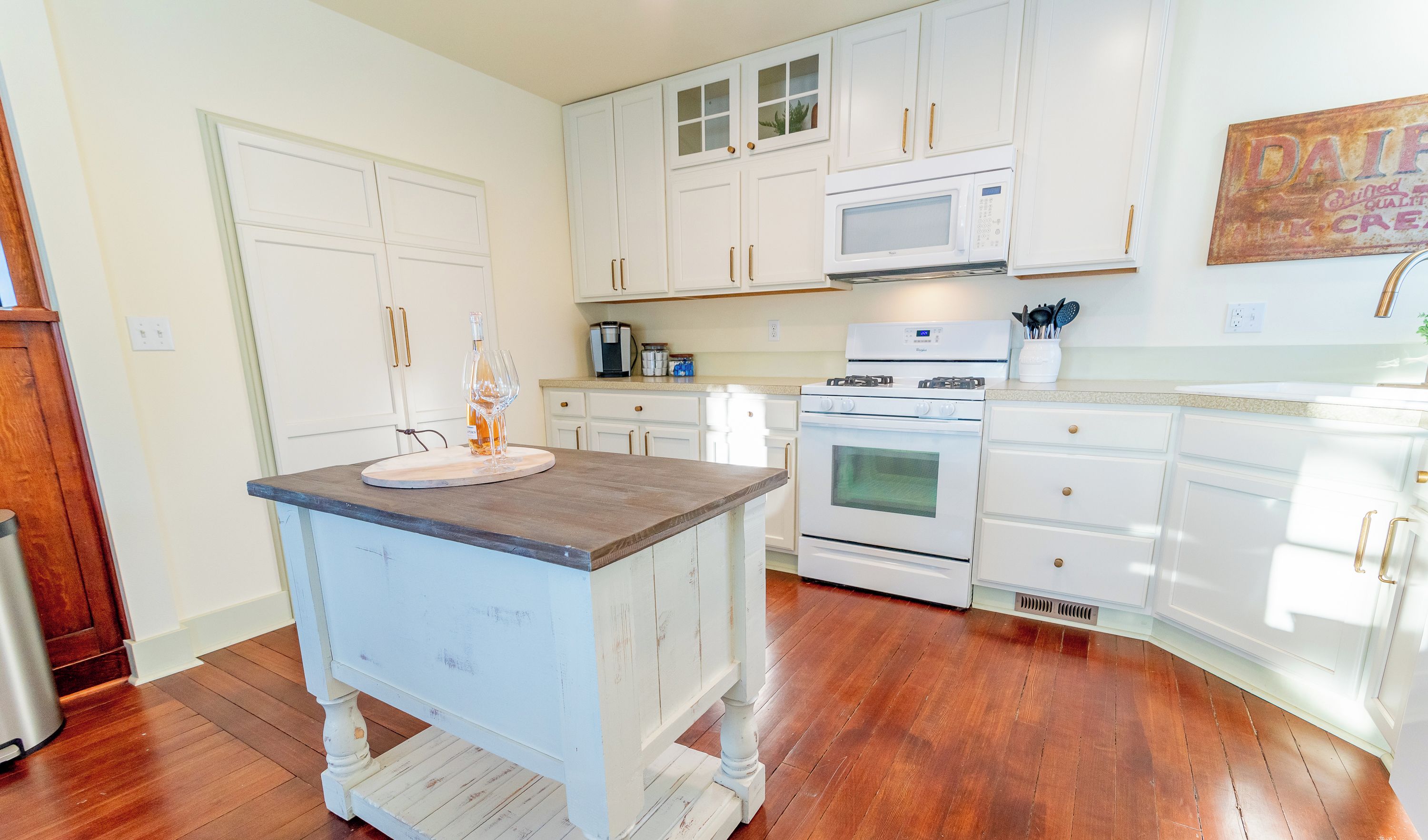 A kitchen with white cabinets, a wooden island, a microwave, and an oven.
