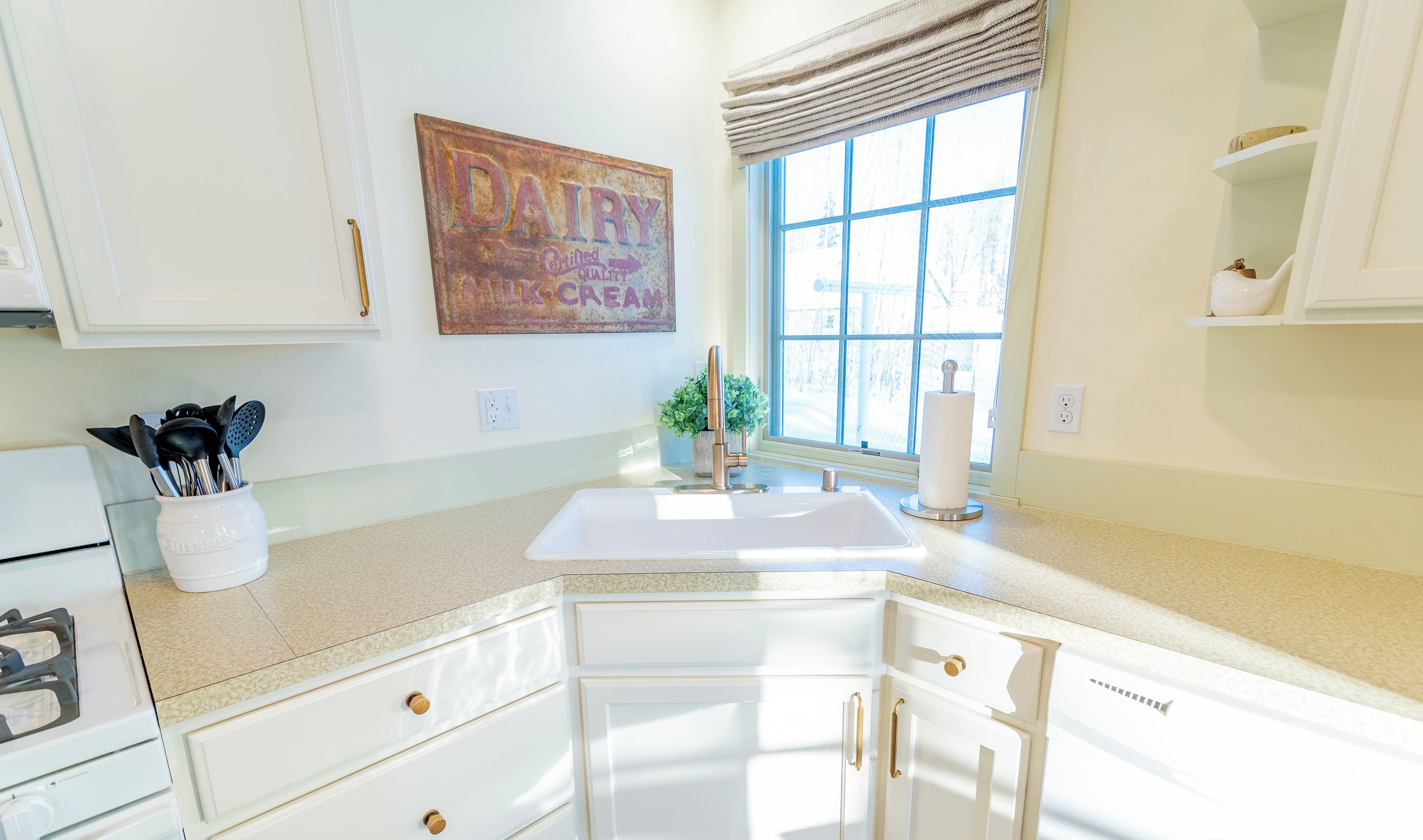 A kitchen with white cabinets, a sink, and a window with blinds.