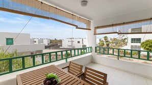 A balcony with a wooden table and chairs, a bowl of fruit, and a view of surrounding buildings.