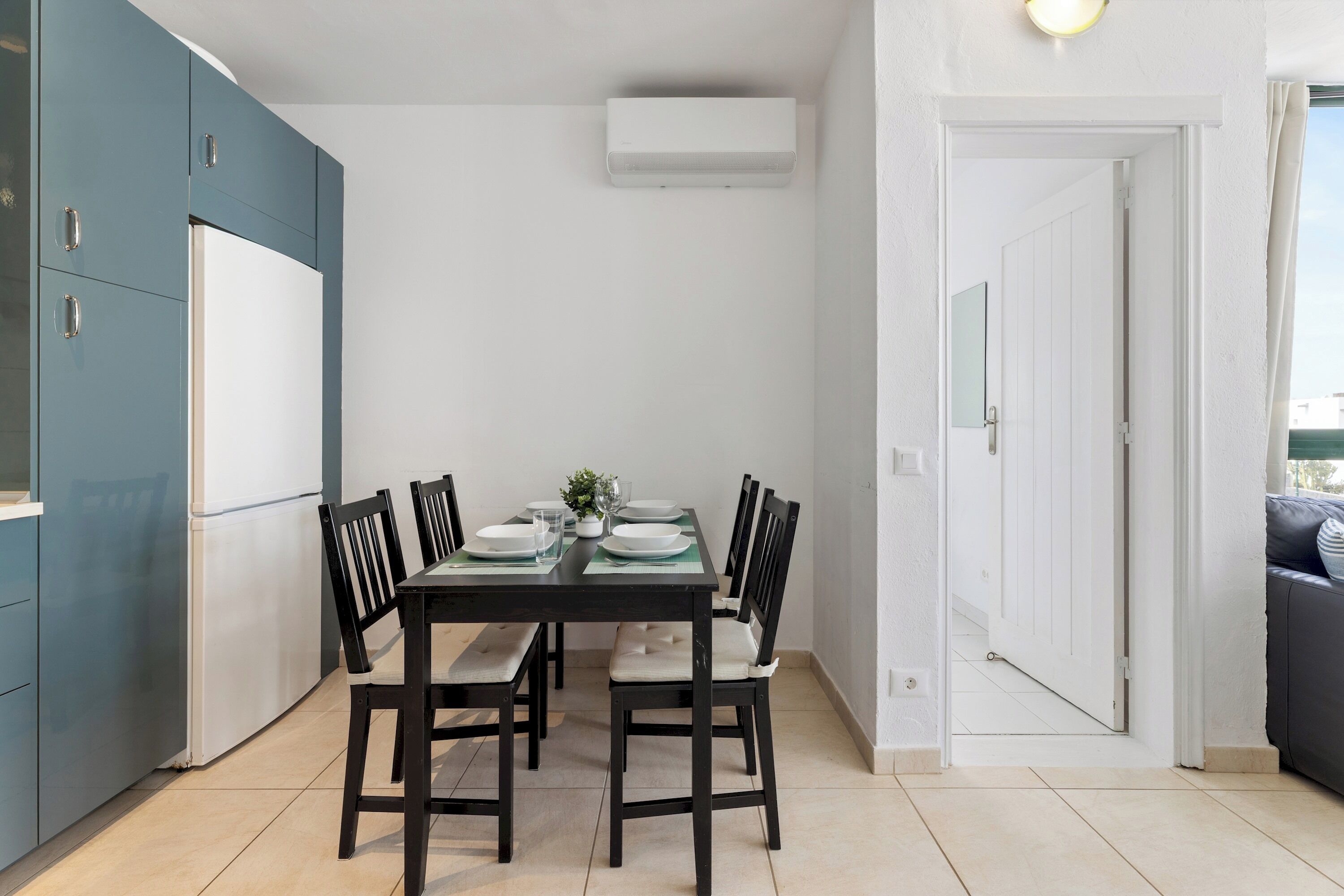 A compact kitchen with teal cabinets, a white refrigerator, and a dining table set for four.
