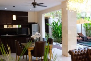 Una cocina moderna con armarios oscuros, una zona de comedor con mesa y sillas, y vista al área de una piscina.