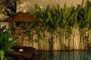 Un espace piscine agrémenté de chaises longues et d’un parasol, entouré de grandes plantes tropicales.