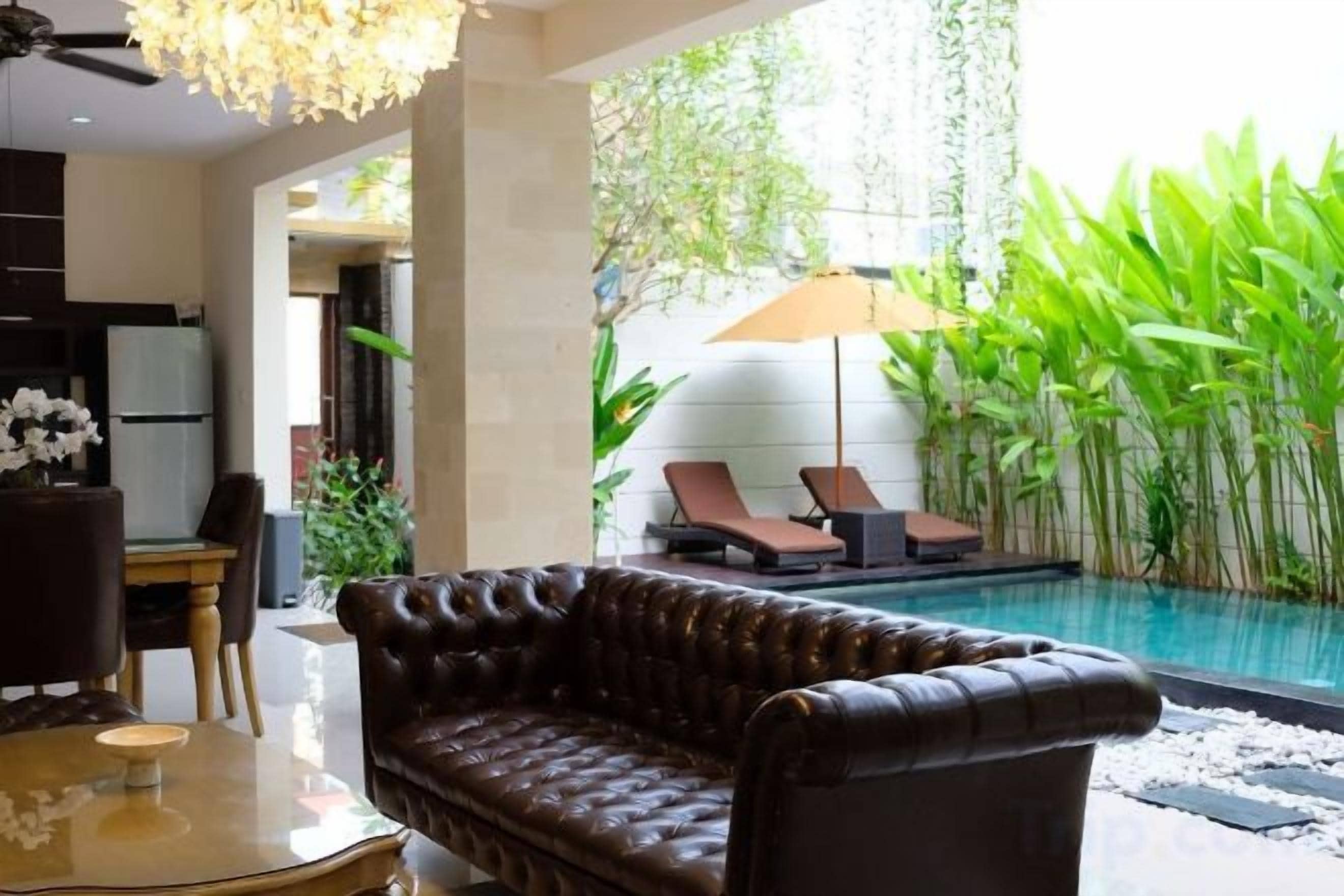 A modern living room with a leather sofa, a dining table, and a view of a swimming pool with lounge chairs.