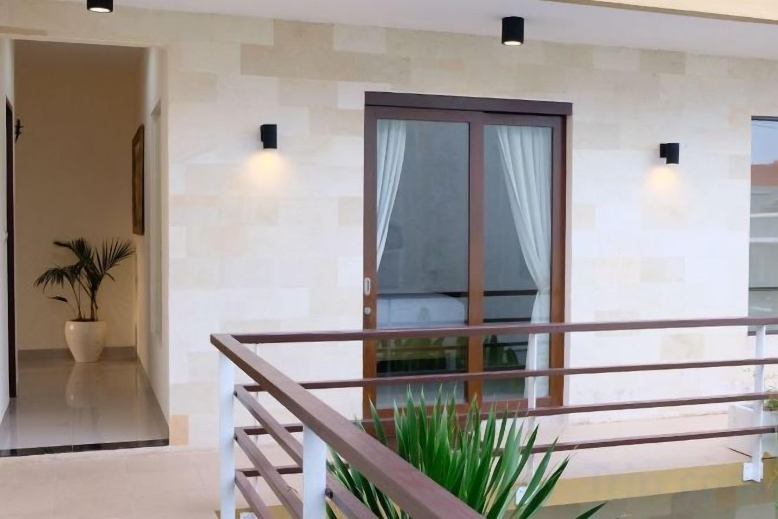A modern interior with a glass door leading to a balcony, a potted plant, and a staircase with a wooden railing.