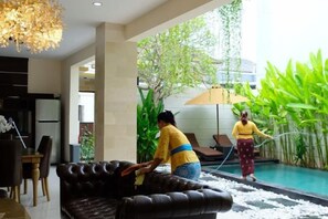 A room with a sofa, a dining table, chairs, and a large window overlooking a pool area. - VIlla Avi (Bali)