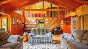 A cozy log cabin interior with a central plaid sofa, two armchairs, a piano, and a staircase leading to an upper level. - Country home in beautiful Bucks County (Hatfield)