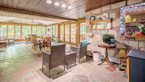A spacious dining area with a large table and wicker chairs, a stone fireplace with a television, and a stone wall with shelves. - Country home in beautiful Bucks County (Hatfield)