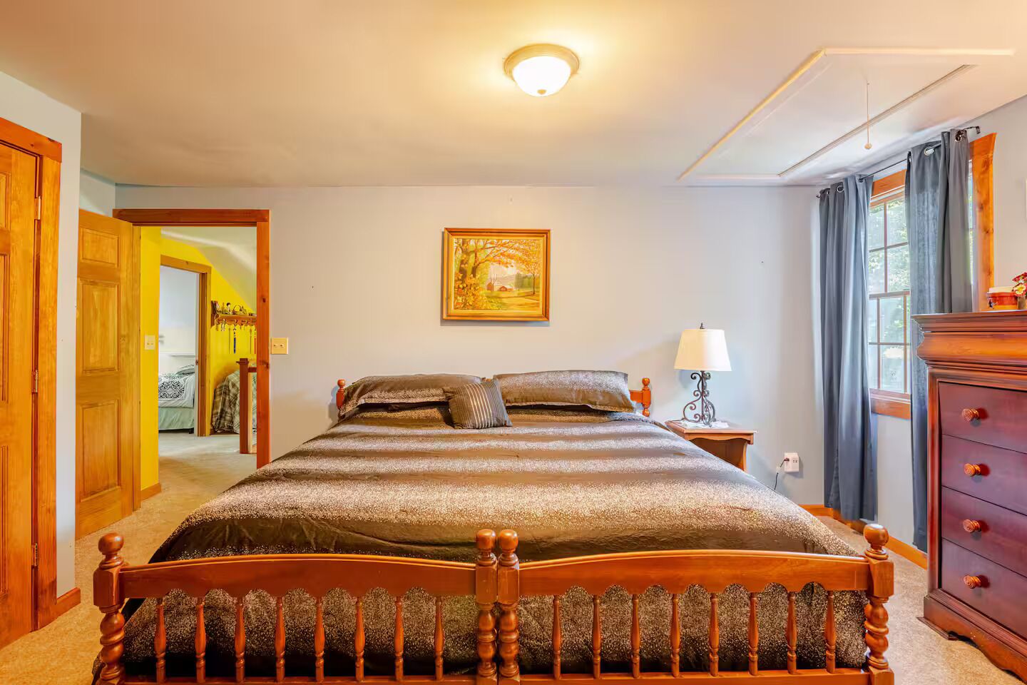 A bedroom with a wooden bed, a nightstand with a lamp, a dresser, and a painting on the wall.
