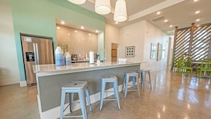 A modern kitchen with a central island, bar stools, a stainless steel refrigerator, and a dining area with green chairs. - Landing Apartments Austin - Lockhart (Lockhart)
