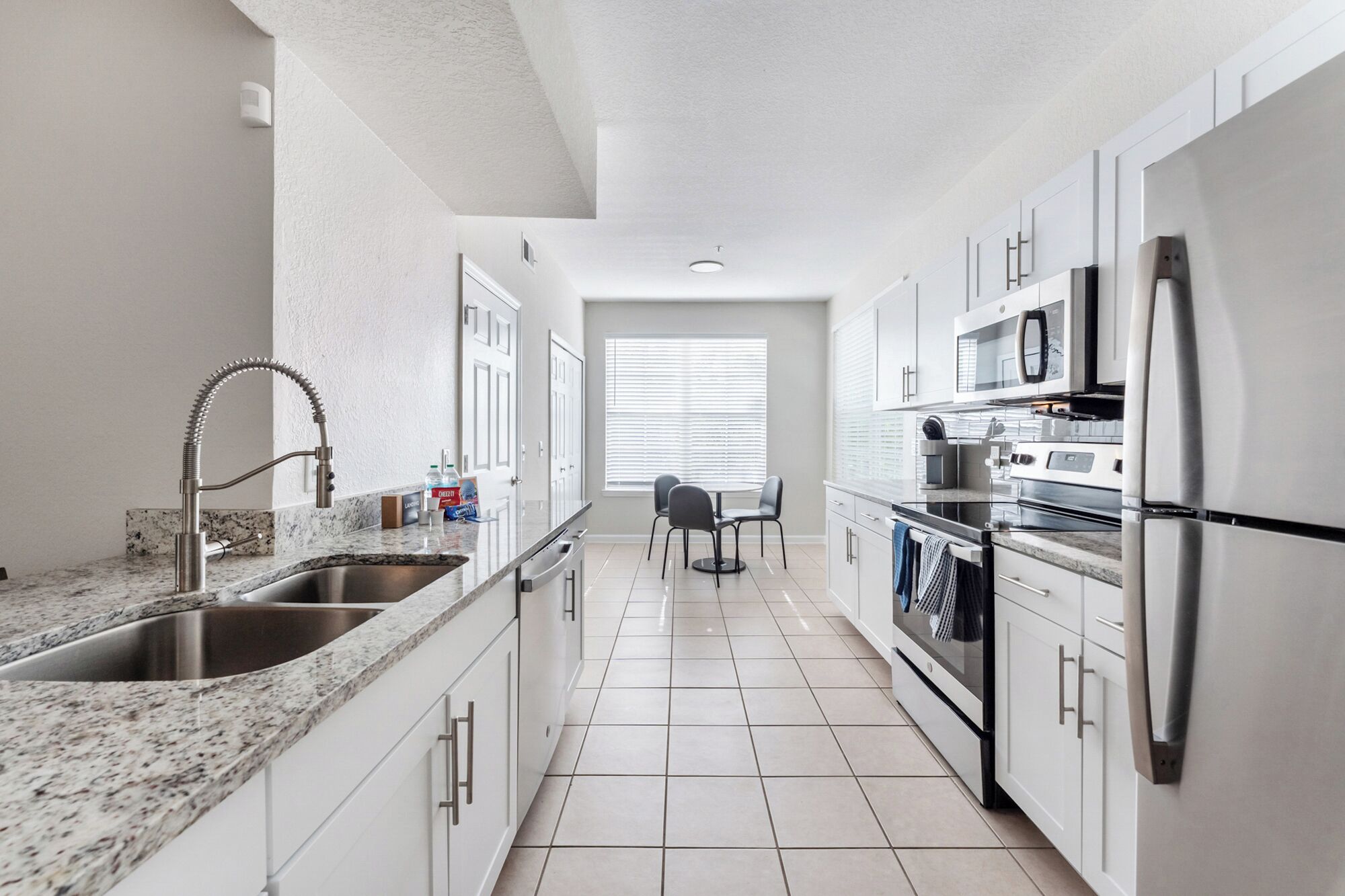 A modern kitchen with a granite countertop, stainless steel appliances, and a dining area with a table and chairs.