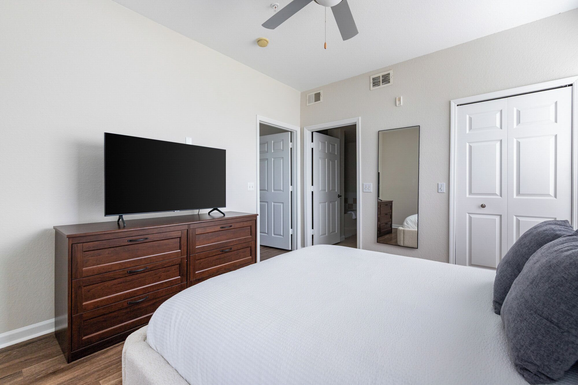 A bedroom with a large bed, a TV on a dresser, a ceiling fan, and white doors.