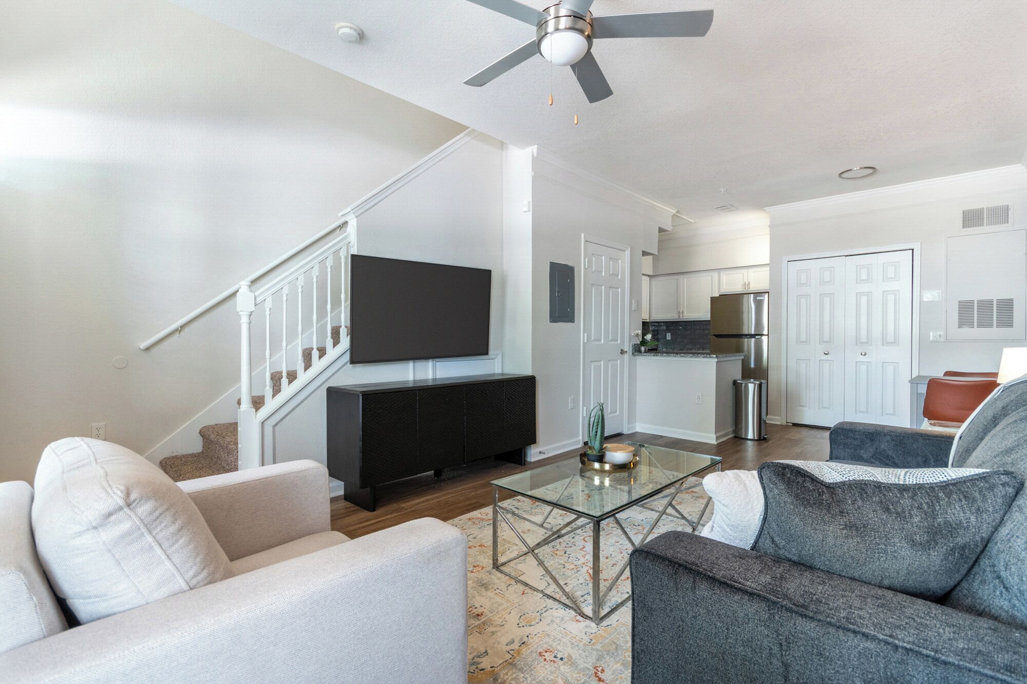 A living room with a flat-screen TV, a glass coffee table, and a staircase.